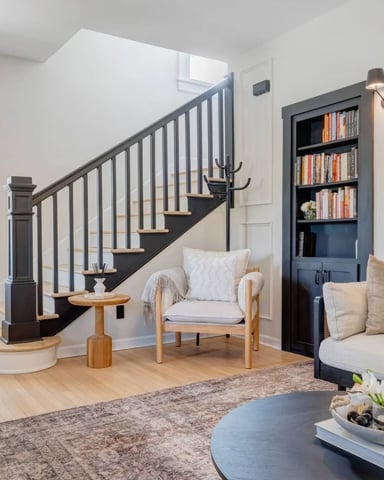 Bright entryway with black staircase, wooden armchair, built-in bookshelf, and cream sofa with blue coffee table