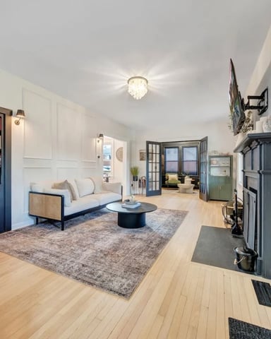 Bright open-plan living room with light wood floors, cream sofa, round black coffee table, blue built-in shelving, and decorative round door with geometric