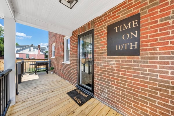Covered wooden deck with red brick exterior, black sign reading "TIME ON 10TH", glass door, and view of neighboring houses