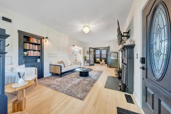 Bright open-plan living room with light wood floors, cream sofa, round black coffee table, blue built-in shelving, and decorative round door with geometric