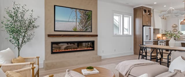 Open-plan living room with fireplace, TV, cream seating, and kitchen visible in background