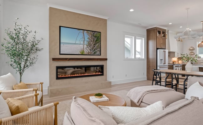 Open-plan living room with fireplace, TV, cream seating, and kitchen visible in background