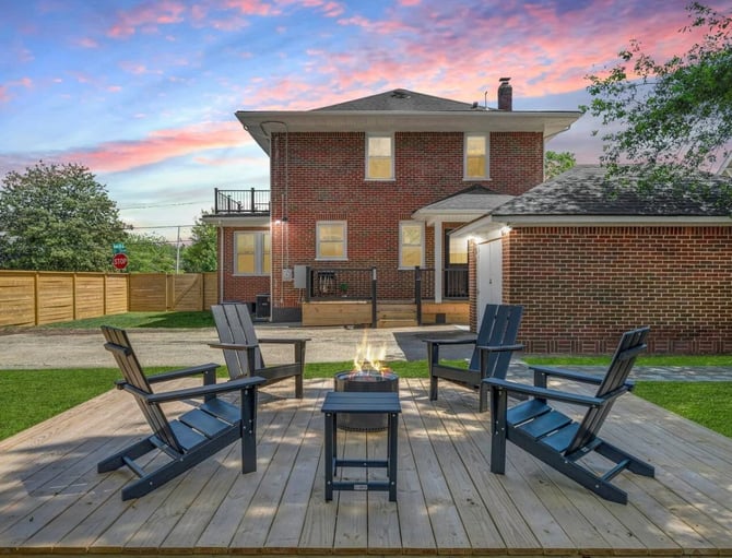 Brick two-story house with wooden deck, fire pit, Adirondack chairs, and fenced yard at sunset